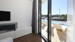 A modern bedroom with a large sliding glass door leading to a pool area. - Homes4You Villas Complex (Kraj)