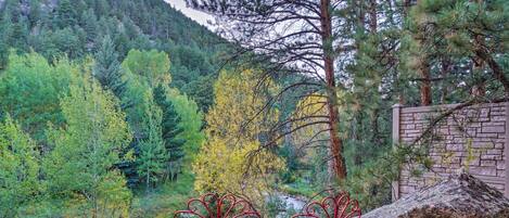 Two red metal chairs with intricate designs, positioned on a rocky surface with a forested mountain backdrop.