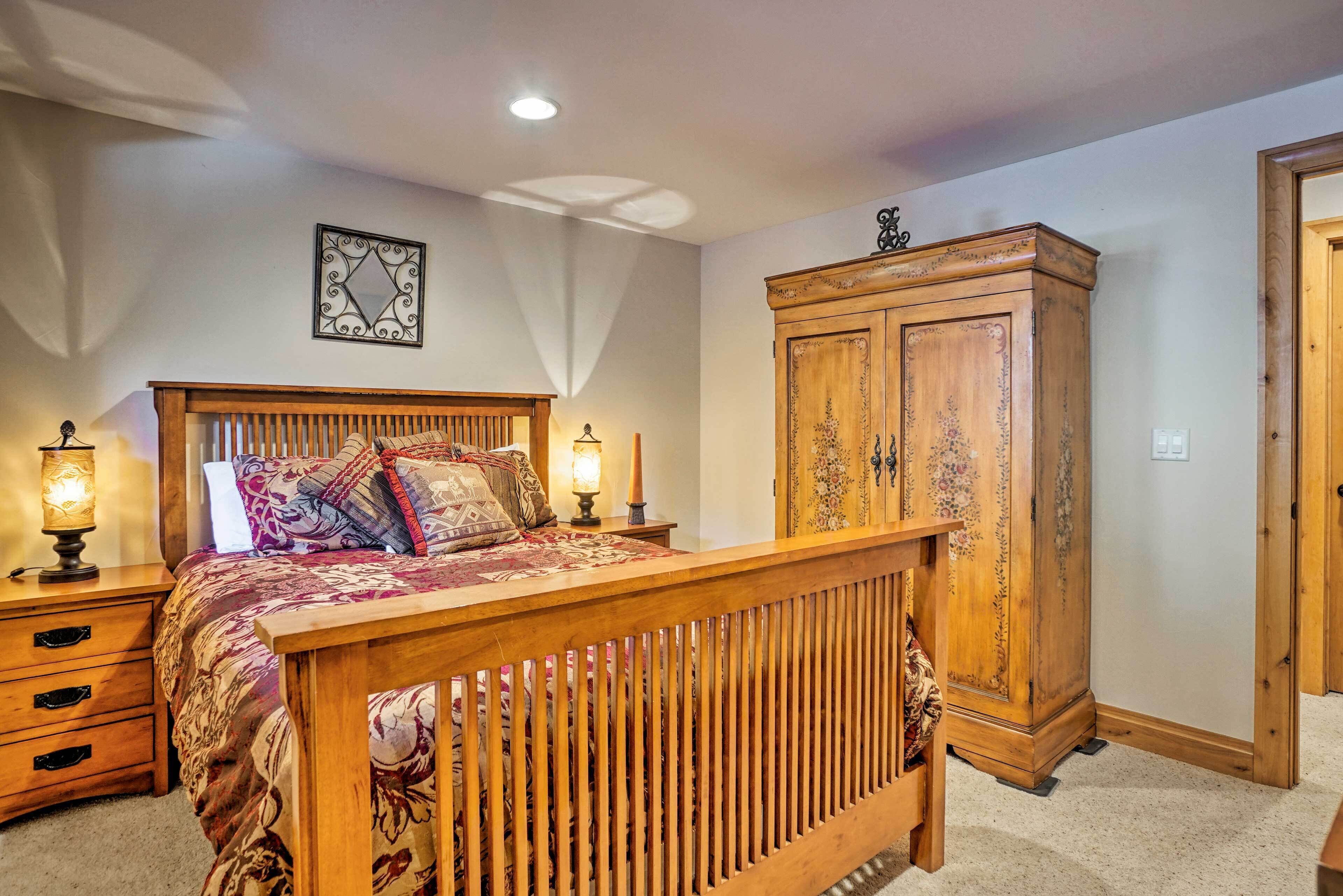 A bedroom with a wooden bed, two bedside lamps, a nightstand, a wooden wardrobe, and a decorative wall piece.