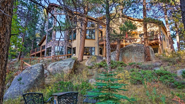 A modern cabin with large windows, surrounded by trees and rocks.