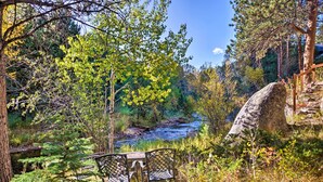 A serene outdoor setting with a wooden bench and a table, surrounded by lush greenery and a flowing stream.