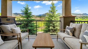 Un balcón con sofá, mesa y parrilla, con vistas a un paisaje montañoso.
