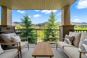 A balcony with a sofa, a table, and a grill, overlooking a mountainous landscape. - Velvet Noir | Lake | Pool | Hot Tub | Gym | Pets (Invermere)