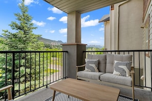 Un balcon avec un canapé et une table, une vue sur les montagnes et un arbre.