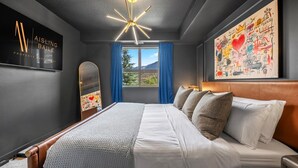 Una habitación de hotel moderna con una cama grande, una lámpara en el techo, una ventana con cortinas y una obra de arte colgada en la pared.