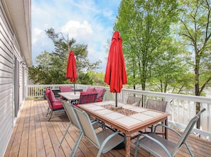 Une terrasse en bois avec une table et des chaises, des parasols rouges et une balustrade blanche.