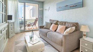A modern living room with a beige sofa, a coffee table, and a TV on a cabinet. There is a balcony with a view of the sea and a painting on the wall. - Port Arcachon by Interhome (Arcachon)
