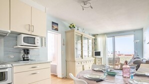 A modern kitchen with a microwave, oven, and coffee maker. There is a dining area with a table set for two, and a view of the city through large windows. - Port Arcachon by Interhome (Arcachon)