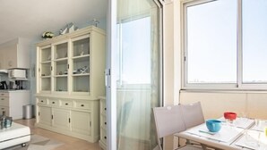 A modern kitchen with white cabinets, a dining area with a table and chairs, and a large window providing natural light. - Port Arcachon by Interhome (Arcachon)