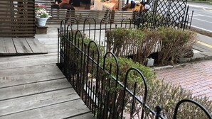 A wooden deck with a metal fence, potted plants, and a building in the background.