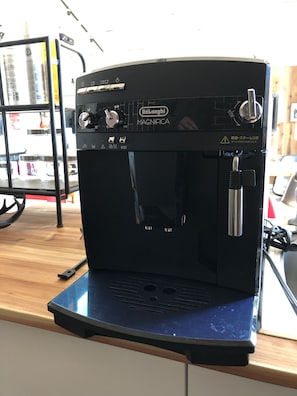 A Delonghi Magnifica espresso machine on a counter with a wooden surface.