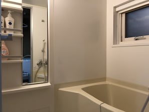 A bathroom with a bathtub, a window, and a shelf with toiletries.