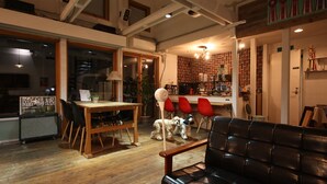 A spacious living area with a wooden dining table, black leather sofa, and a dog.