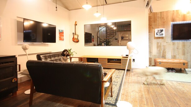A modern living room with a black leather sofa, a flat-screen TV, a guitar, and a wooden bench.