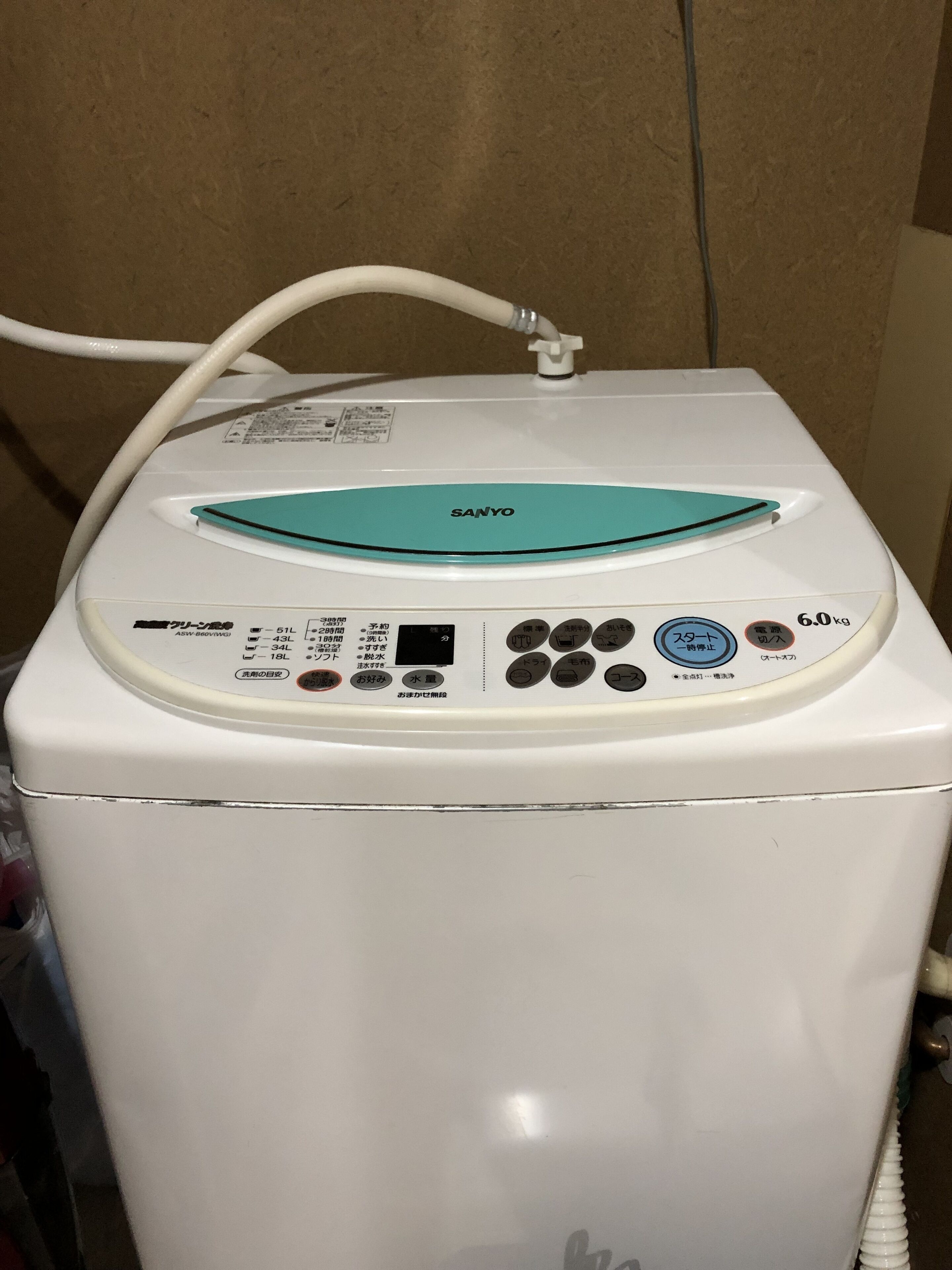 Máquina de lavar roupa branca com painel de comandos, rótulo de capacidade de 6,0 kg e cabo de alimentação ligado.