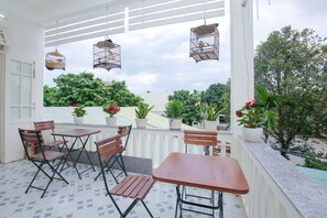 A balcony with a wooden table and chairs, potted plants, and hanging birdcages. - Van May Homestay Hoian (Da Nang)