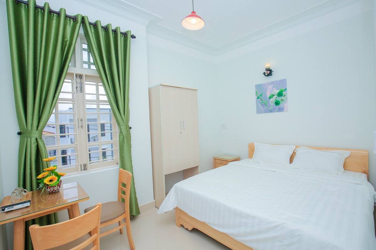 A bedroom with a bed, a desk with a chair, a wardrobe, and a window with curtains.