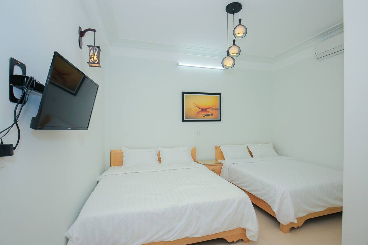 A hotel room with two single beds, a flat-screen TV mounted on the wall, and a framed picture on the wall.