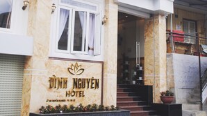 A building with a sign for Dinh Nguyen Hotel, featuring a marble facade, a staircase leading to the entrance, and a small garden area.