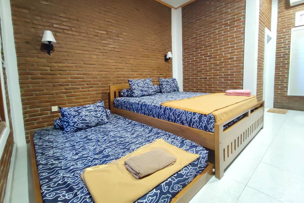 A room with two beds, a brick wall, and a white door.