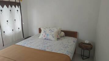 A bedroom with a bed, floral bedding, a wooden headboard, a nightstand, and a curtain with a geometric pattern.