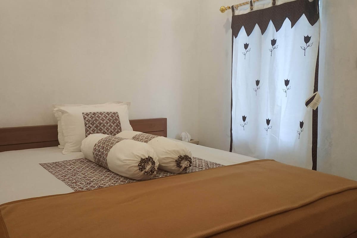 A neatly made bed with a brown bedspread and patterned pillows, a wooden headboard, and a white wall.