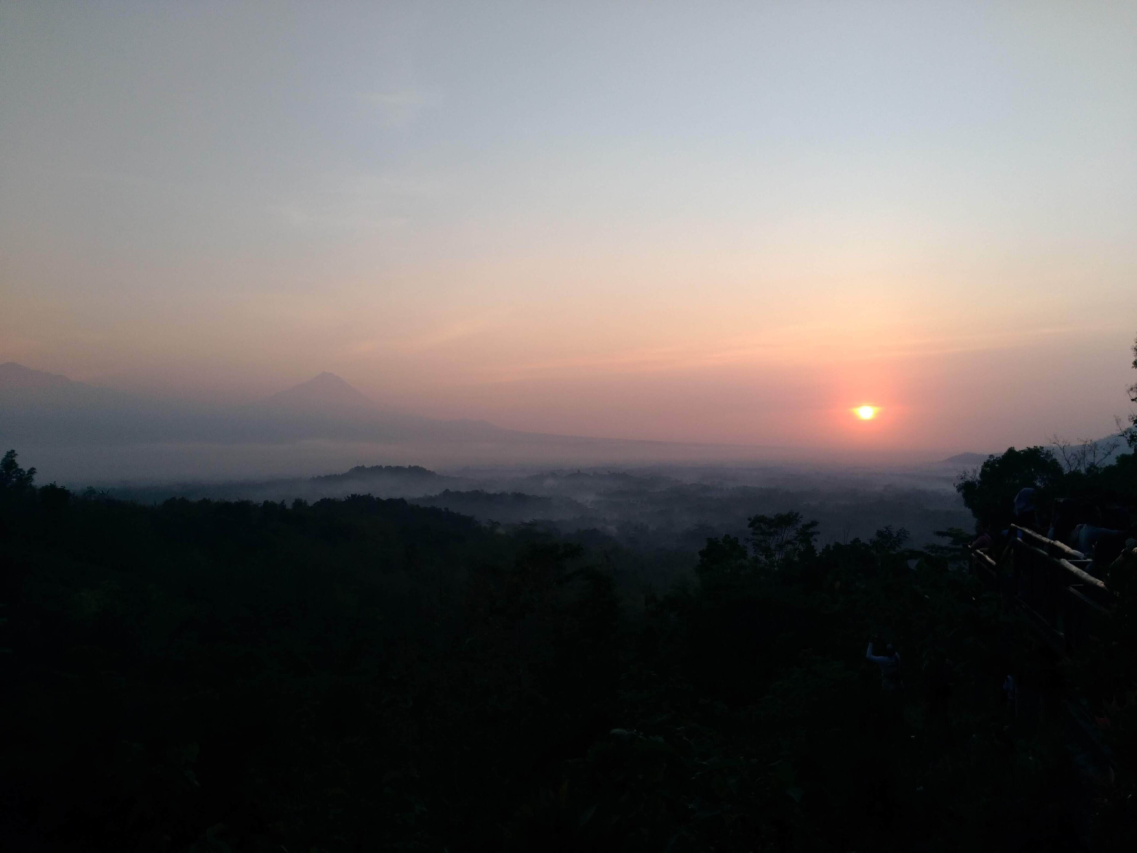 A sunrise over a mountainous landscape with a view of the sun rising over the horizon.