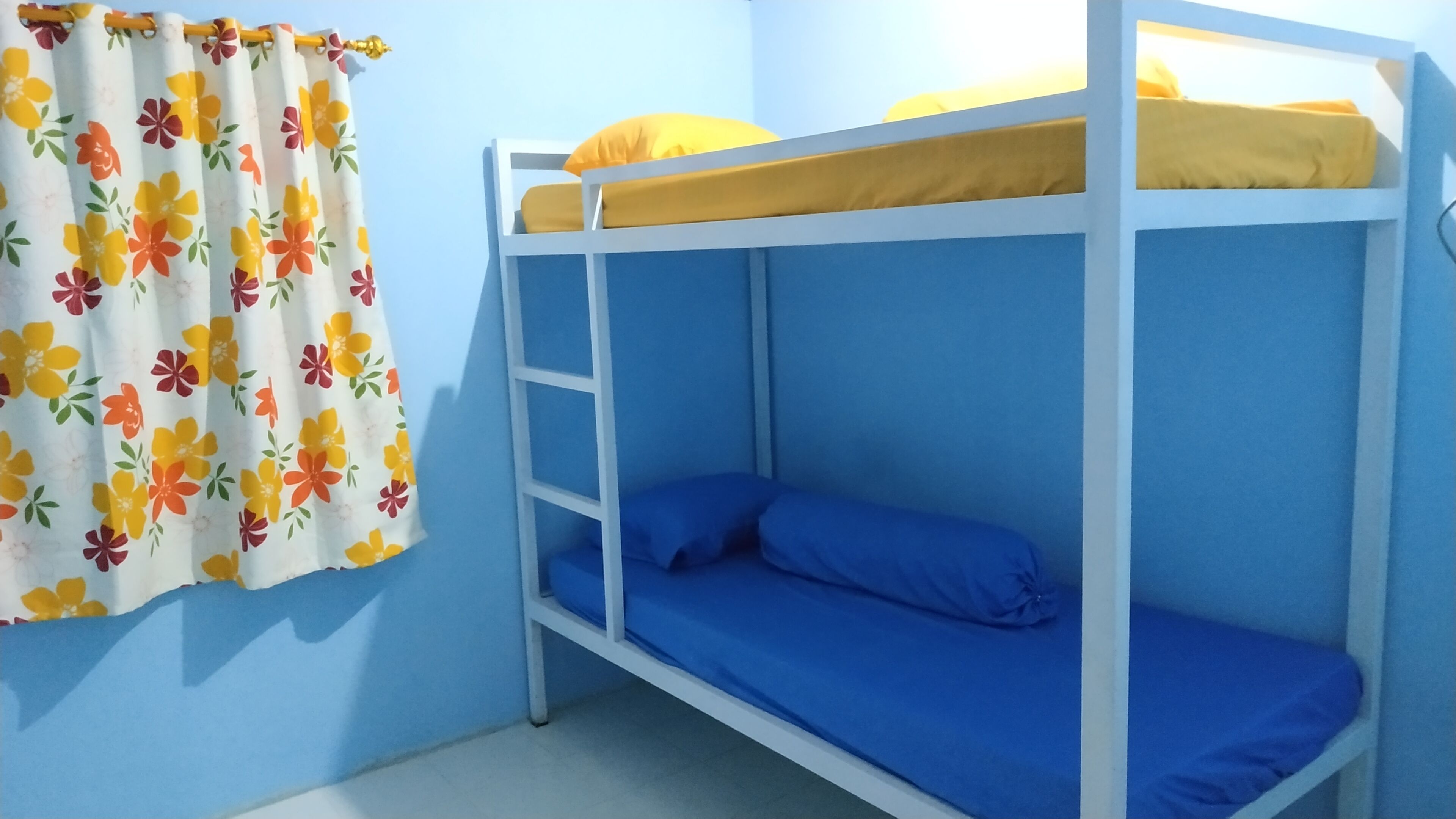 A bunk bed with a blue mattress and a yellow pillow, a floral curtain, and a blue wall.