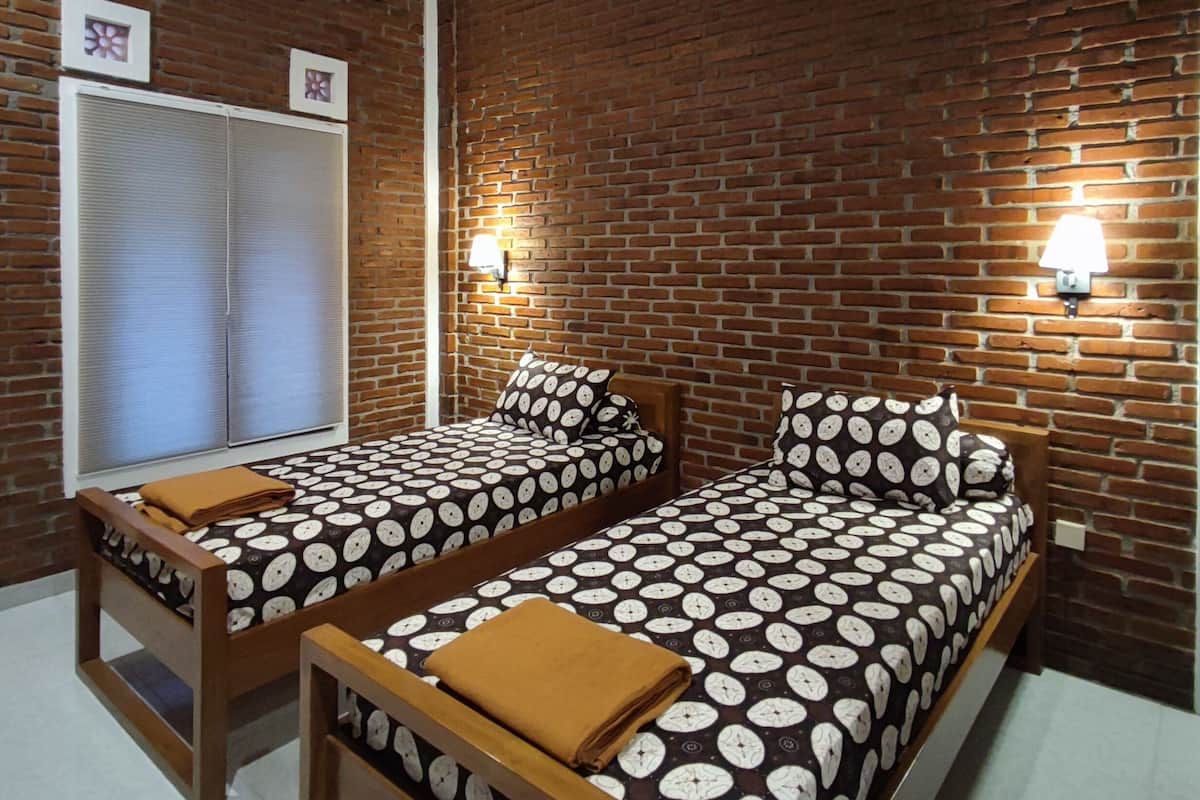 A room with two beds, a brick wall, and a window with blinds.