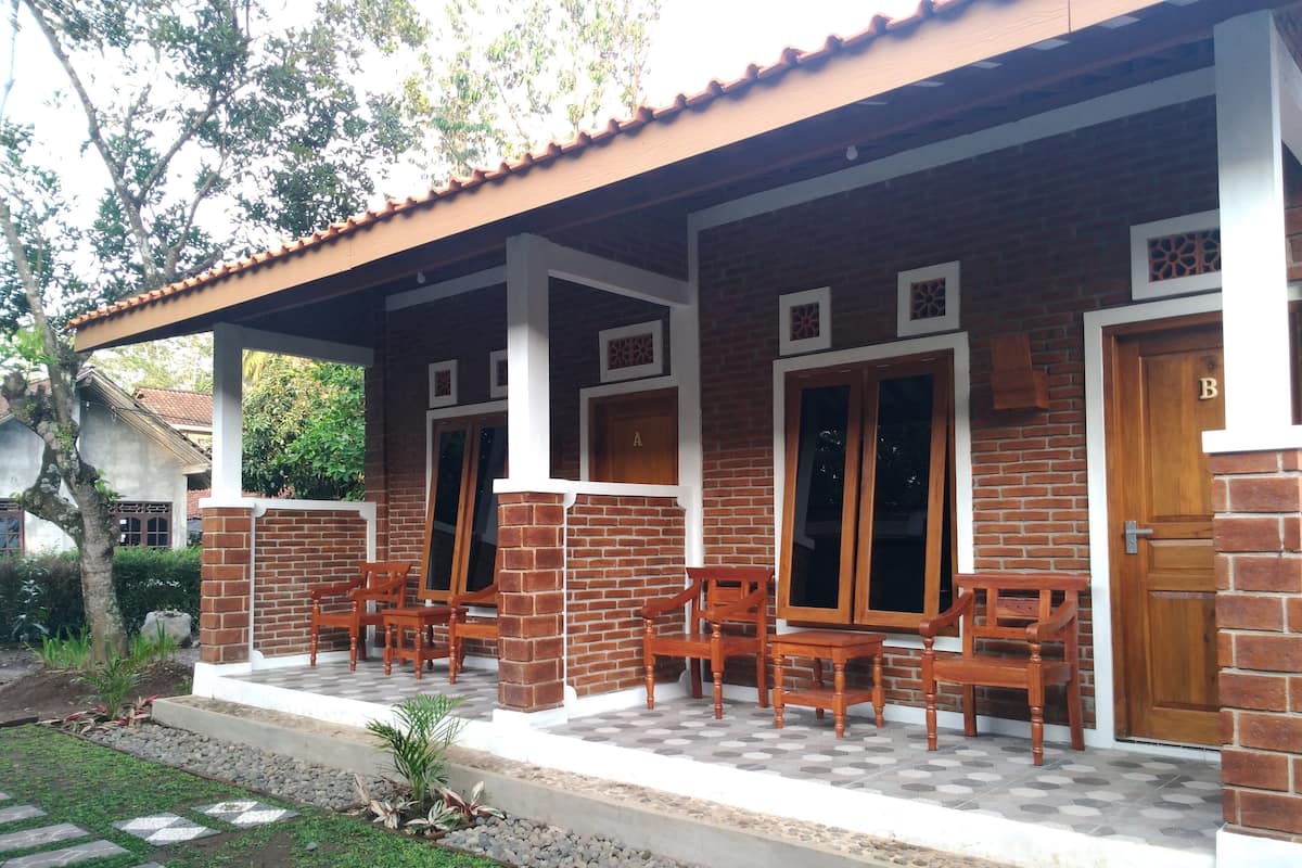 A brick house with a tiled porch, wooden chairs, and a door marked 'B'.