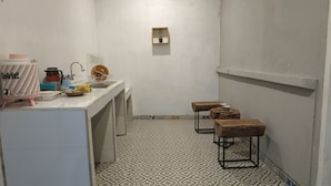 Et lille, rent badeværelse med håndvask, spejl og toilet. Der er træbænke og en lille hylde med en plante.