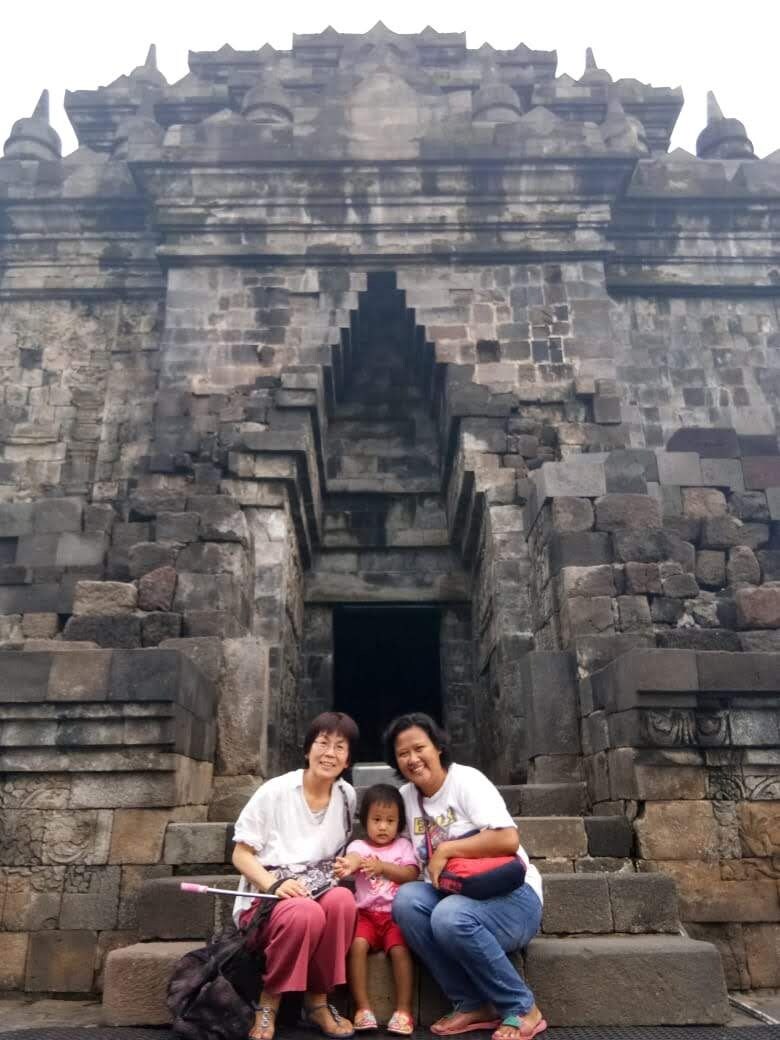 A family sitting on stone steps in front of a temple entrance with a tiered roof.