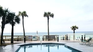 A swimming pool with a view of the ocean, surrounded by palm trees and a fence.