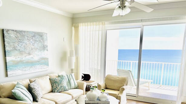A spacious living room with a beige sofa, a coffee table, and a view of the ocean through large sliding doors.