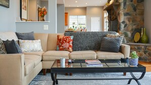 Una sala de estar con un sofá color beige, una mesa de centro de vidrio y una chimenea de piedra.