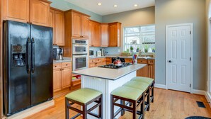 Una cocina moderna con armarios de madera, un refrigerador negro, electrodomésticos de acero inoxidable y una isla central con taburetes de bar.