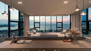 A modern interior with a large panoramic window overlooking a cityscape and water. There are multiple seating areas with chairs and tables, and a bar area with stools. - Pony's Homestay -The Base Condo- (Bang Lamung)