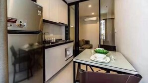 A compact kitchen with a refrigerator, a dining table with chairs, and a glass partition separating the kitchen from a living area. - Pony's Homestay -The Base Condo- (Bang Lamung)