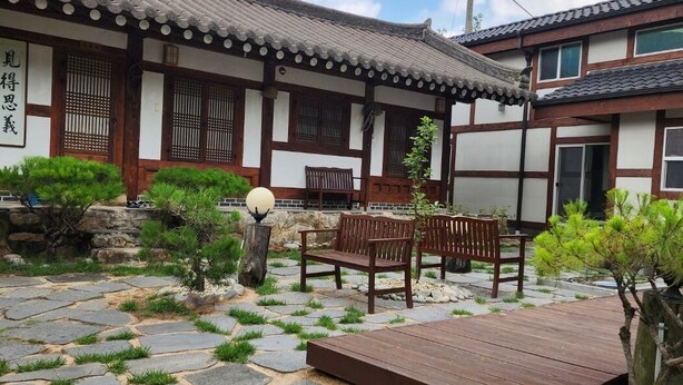 Un edificio japonés tradicional con tejado de tejas, vigas de madera y un sendero de piedra que conduce a una terraza de madera con bancos.