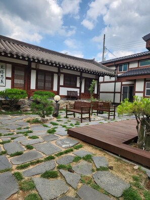 A traditional Japanese building with a tiled roof, wooden beams, and a stone pathway leading to a wooden deck with benches.