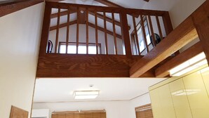 Una habitación con techos altos, vigas de madera a la vista, un banco empotrado y un ventanal grande.