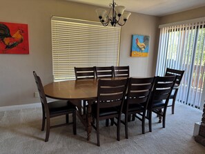 A dining room with a round table and six chairs, a chandelier, and two paintings on the walls.