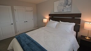 Quarto bem arrumado com uma cama grande, duas luminárias de cabeceira, uma cabeceira e uma obra de arte na parede.