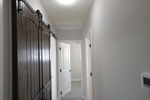 A narrow hallway with a wooden door on the left and a white door at the end. - EXQUISITE 3BD HOUSE CLOSE TO AIRPORT, PL HOSP, DOWNTOWN, SLEEPS 7 (Calgary)