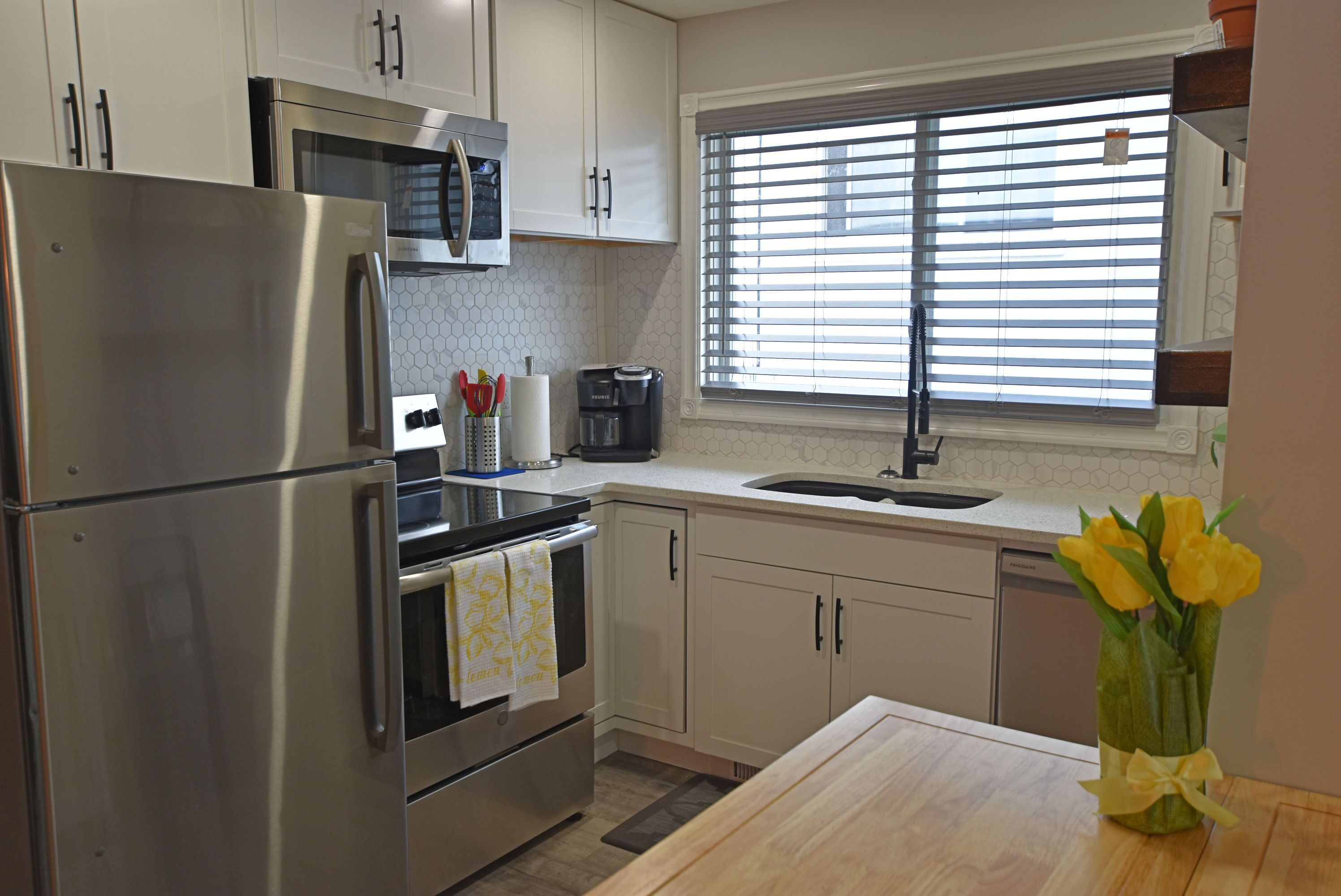 A modern kitchen with stainless steel appliances, a microwave, and a window with blinds.