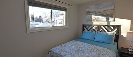A bedroom with a bed, a window, a painting, and a nightstand.
