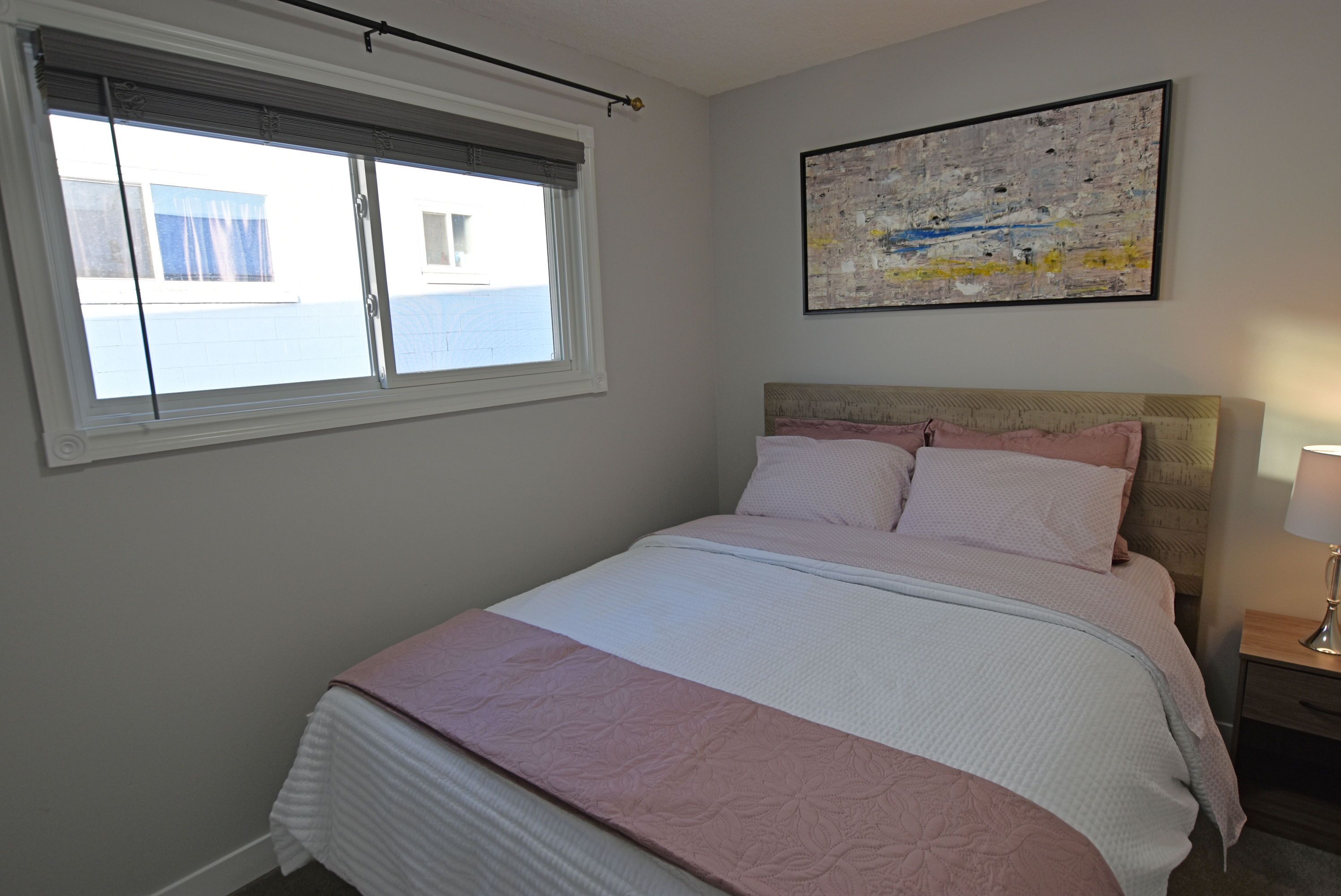 Une chambre à coucher avec un lit, une fenêtre, un tableau et une table de chevet.