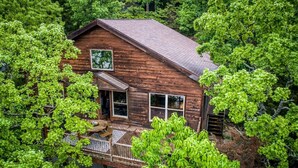 A wooden cabin surrounded by dense green foliage. - Free Night: Make Ozarks Memories at this Custom Lakefront Post & Beam Home VIDEO (Eldon)