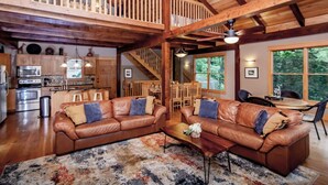 A spacious living area with a high ceiling, wooden beams, a kitchen with modern appliances, and a dining area with natural light. - Free Night: Make Ozarks Memories at this Custom Lakefront Post & Beam Home VIDEO (Eldon)