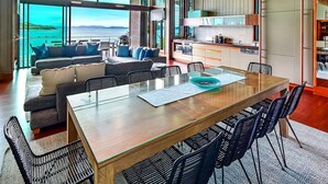 Un interior moderno con comedor, cocina y zona de estar junto a un amplio ventanal con vistas al agua.